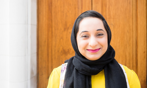 A woman in a hijab smiling to camera in front of an orange door